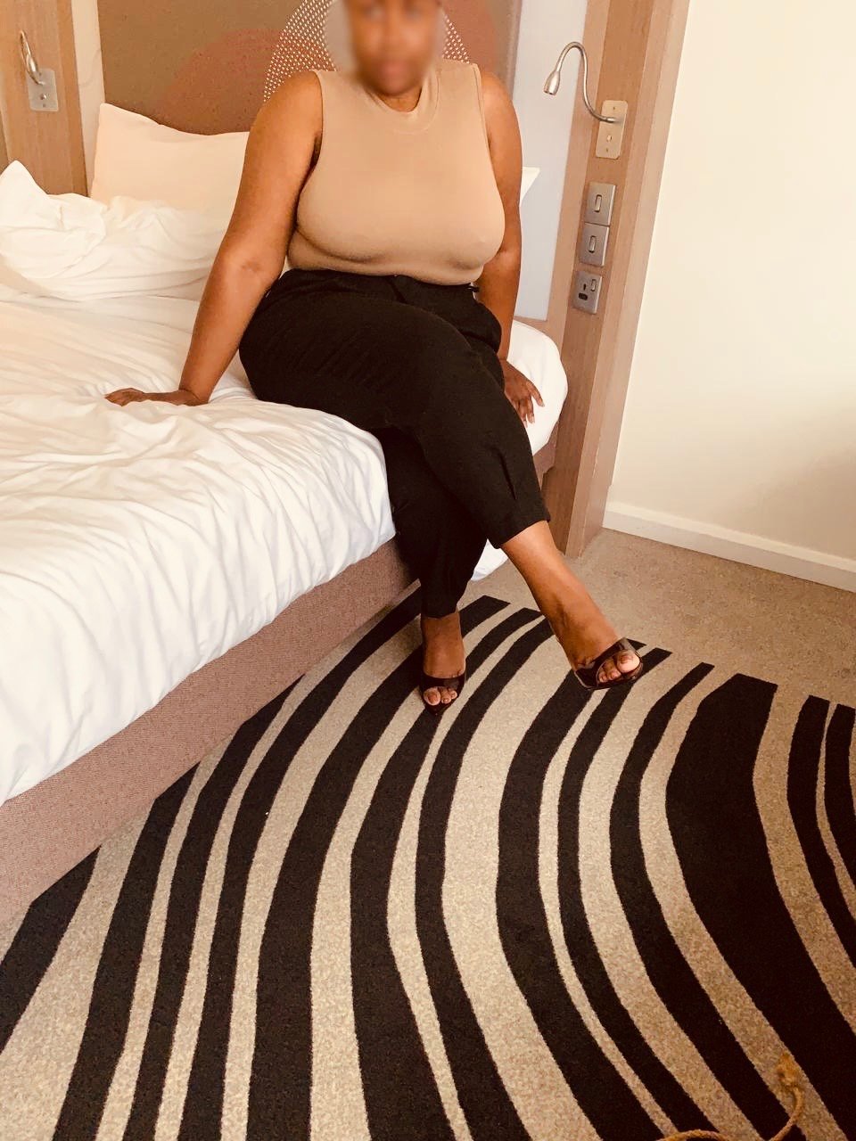 A pair of crossed legs in heels fishnets and heels sitting on a grey chair. Sable Gold, Luxembourg escort